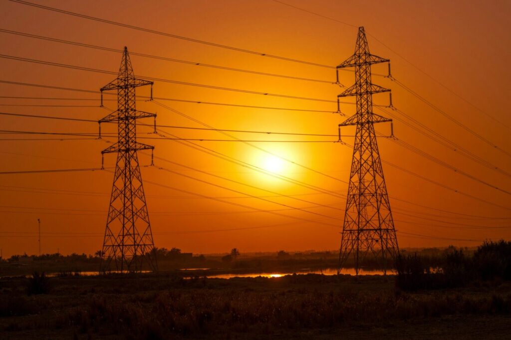 Silhouetted transmission towers under a vibrant sunset in Baghdad, Iraq.