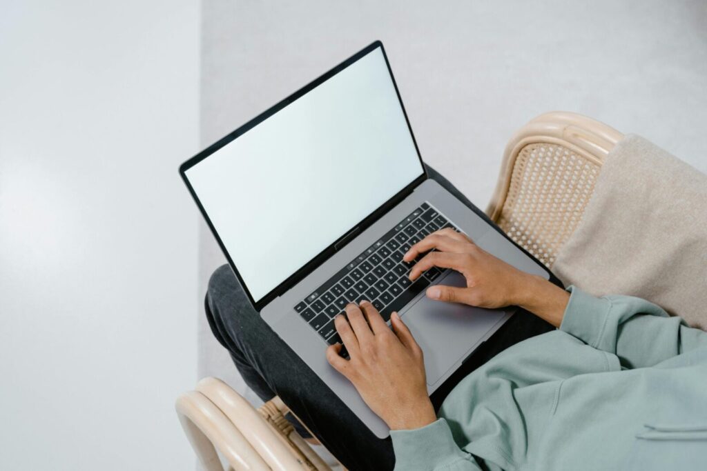 Overhead view of a person typing on a laptop in a comfortable armchair indoors.